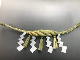 A rice straw rope tapering at each side with three tassels. Four paper zigzags hang alternating with the tassels.